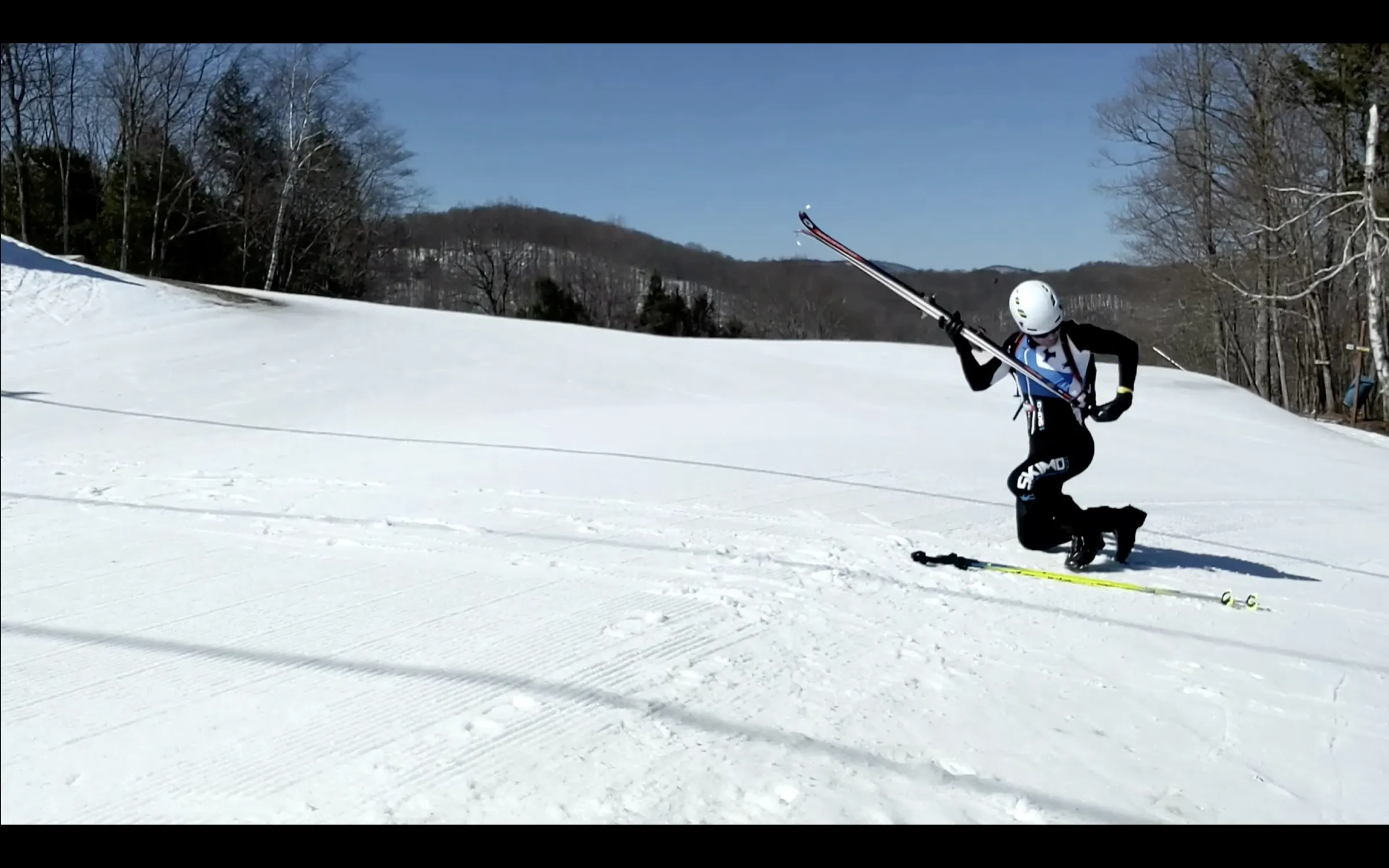 A photo of a skimo racer on one knee and holstering skis